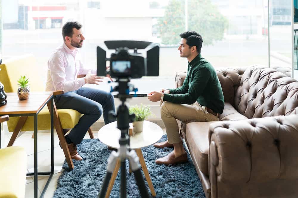 journalist interviewing businessman while recording in video camera at office